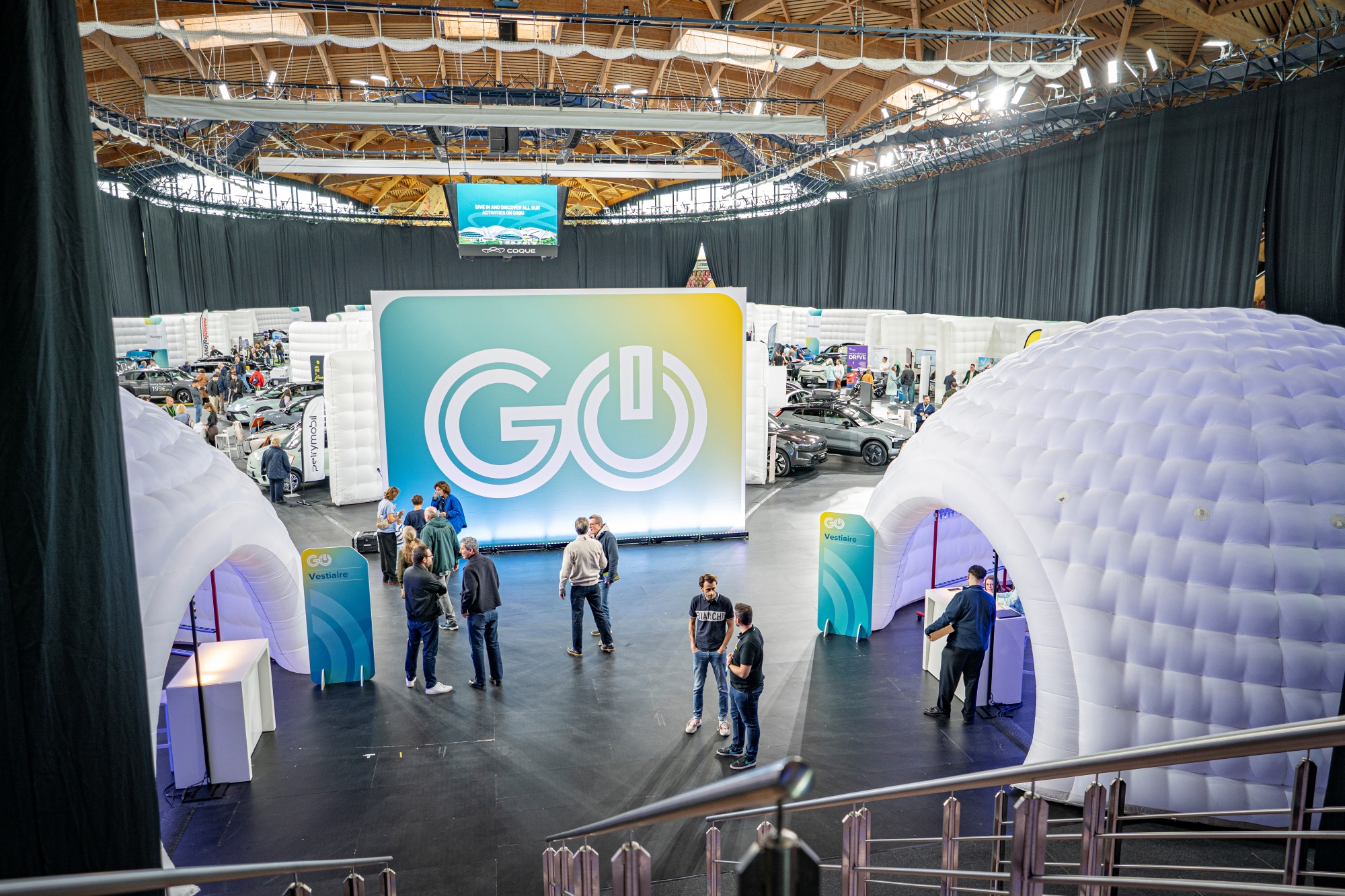 Vue sur l’événement GO Electric Day à la Coque, avec des structures gonflables blanches et un grand panneau “GO”, où les visiteurs échangent et se renseignent.