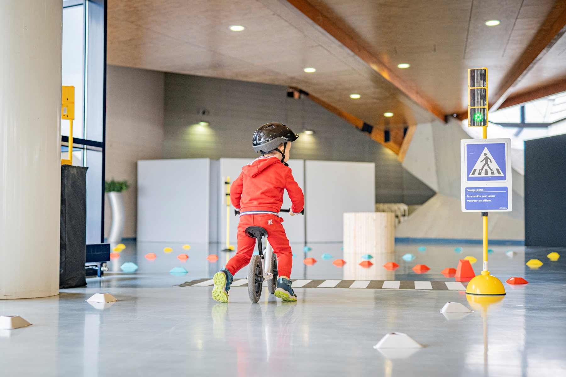Un enfant portant un casque et une tenue rouge participe à un parcours d’apprentissage de la sécurité routière sur un vélo d’équilibre au GO electric day.